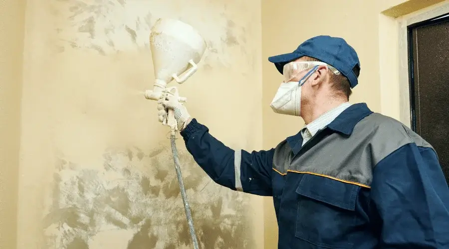 man spray painting walls while wearing protective face and mask gear